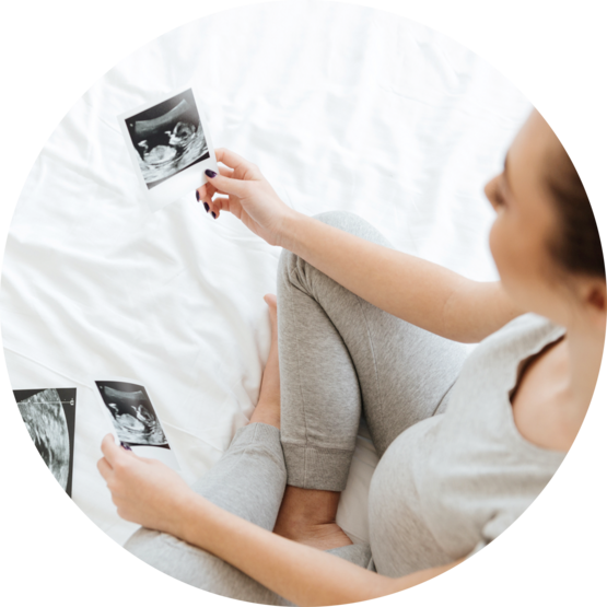 Pregnant woman sitting on a bed, looking at ultrasound images with a peaceful expression, reflecting on her pregnancy.