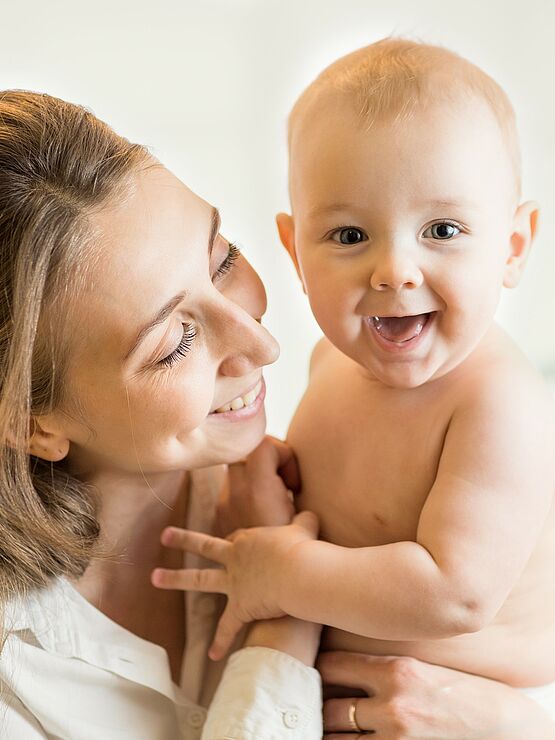 Smiling mother holding her happy baby, who is looking at the camera, both enjoying a tender moment