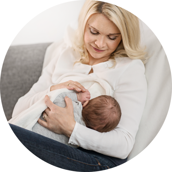 Mother sitting on a couch and breastfeeding her baby, looking down with a gentle smile