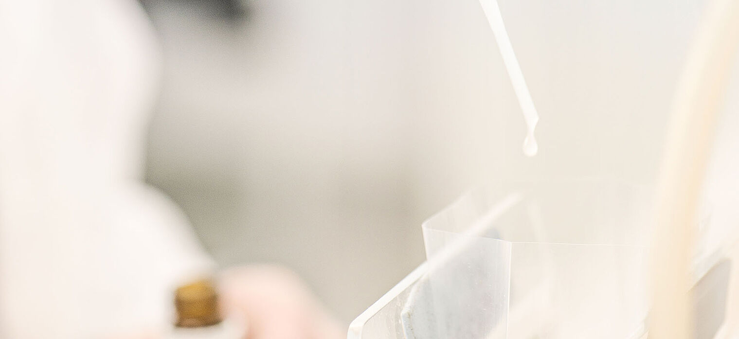 Close-up of a laboratory setting with a pipette dispensing a liquid into a clear container.