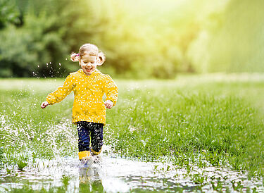 A blonde smiling girl with a white dotted yellow rain jacket